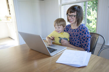 Lächelnde Mutter mit Sohn, der einen Laptop auf einem Tisch zu Hause benutzt - CAVF48859