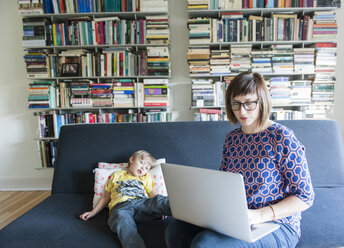 Mutter benutzt einen Laptop, während sie mit ihrem Sohn zu Hause auf dem Sofa sitzt - CAVF48863