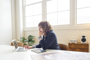 Geschäftsfrau, die einen Laptop benutzt, während sie am Schreibtisch im Büro sitzt - CAVF48868