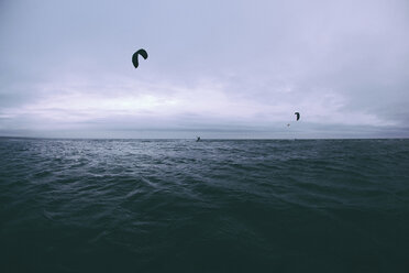 Menschen Kiteboarding über Meer gegen bewölkten Himmel - CAVF48873