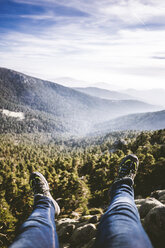 Low section of man sitting on landscape against cloudy sky - CAVF48898