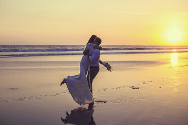Newlywed couple embracing at beach against clear sky during sunset - CAVF48902