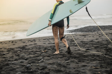Tiefschnitt einer Frau, die ein Surfbrett hält, während sie bei Sonnenuntergang am Strand spazieren geht - CAVF48914