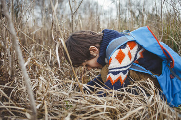 Side view of boy with backpack crouching on grassy field - CAVF48926