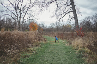 Happy boy with arms outstretched running on grassy field against sky in forest - CAVF48927