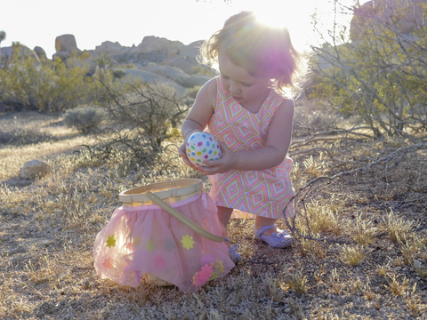 Baby-Mädchen hält bunte Ostereier, während sie auf einer Wiese vor dem Himmel steht, lizenzfreies Stockfoto