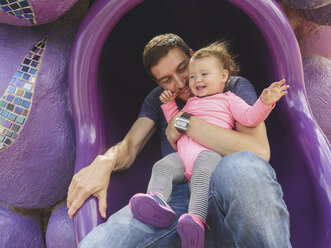 Vater mit niedlicher Tochter auf Röhrenrutsche auf Spielplatz spielend - CAVF48942