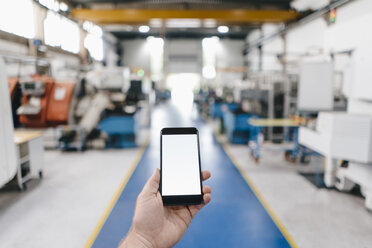 Hand holding smartphone with blank screen in a factory workshop - KNSF04809