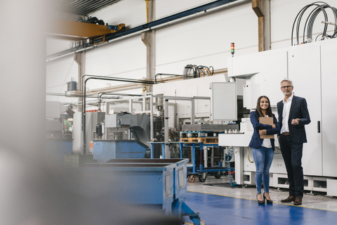 Businessman an woman in high tech enterprise, having a meeting in factory workshop stock photo