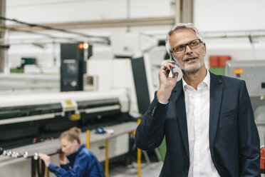 Ein Manager telefoniert, während ein Arbeiter im Hintergrund arbeitet - KNSF04853