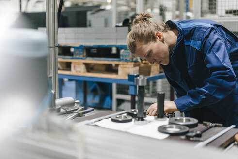 Junge Frau, die als Facharbeiterin in einem High-Tech-Unternehmen arbeitet und eine Produktionsmaschine steuert - KNSF04856