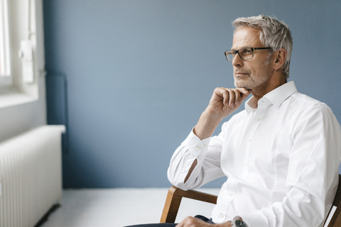 Ein Manager sitzt in seinem Büro, schaut aus dem Fenster und denkt nach, lizenzfreies Stockfoto