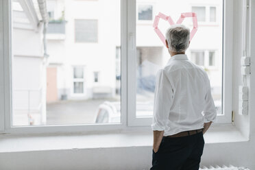 Businessman looking out of a window with a heart-shape on it, rear view - KNSF04875