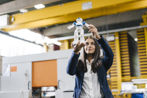 Young woman working in distribution warehouse, looking at toy robot - KNSF04884