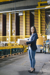 Young woman working at parcel service, carrying parcel in warehouse - KNSF04887