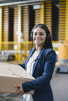Young woman working at parcel service, carrying parcel in warehouse - KNSF04889