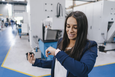 Confident woman working in high tech enterprise, using smartwatch for a call - KNSF04904