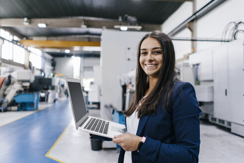 Confident woman working in high tech enterprise, holding laptop - KNSF04905