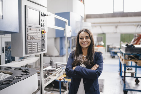Confident woman working in high tech enterprise, standing in factory workshop with arms crossed - KNSF04909