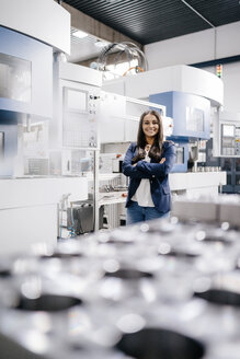 Confident woman working in high tech enterprise, standing in factory workshop with arms crossed - KNSF04910