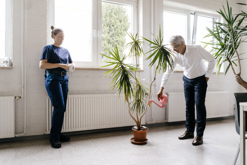 Manager watering plants in recreation room, while worker is drinking coffee - KNSF04930