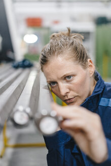 Junge Frau, die als Facharbeiterin in einem High-Tech-Unternehmen arbeitet und Stahlstangen kontrolliert - KNSF04933