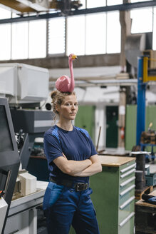 Young woman working as a skilled worker in a high tech company, balancing a pink flamingo on her head - KNSF04953