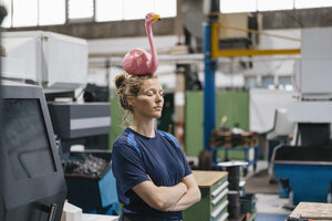 Junge Frau, die als Facharbeiterin in einem High-Tech-Unternehmen arbeitet und einen rosa Flamingo auf dem Kopf balanciert - KNSF04954