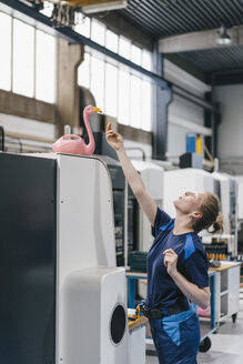 Young woman working as a skilled worker in a high tech company, playing with a pink flamingo - KNSF04955