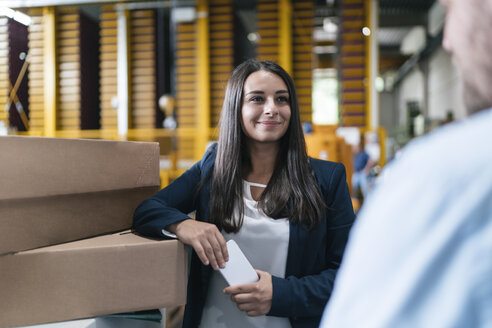 Young woman working in distribution warehouse, talking to colleague - KNSF04962