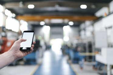 Hand holding laptop with blank screen in a factory workshop - KNSF04976