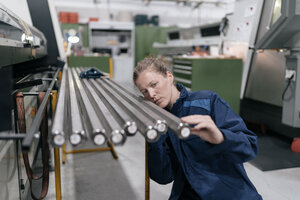 Junge Frau, die als Facharbeiterin in einem High-Tech-Unternehmen arbeitet und Stahlstangen kontrolliert - KNSF04980