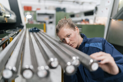 Young woman working as a skilled worker in a high tech company, checking steel rods - KNSF04981