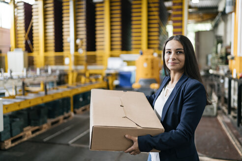 Junge Frau arbeitet bei einem Paketdienst und trägt ein Paket in einem Lagerhaus - KNSF04993