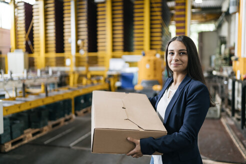 Young woman working at parcel service, carrying parcel in warehouse - KNSF04993