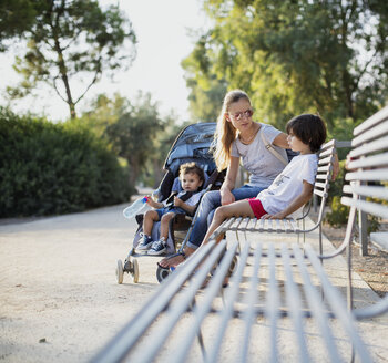 Mutter sitzt auf einer Parkbank und spricht mit einem ihrer Söhne - AZOF00058
