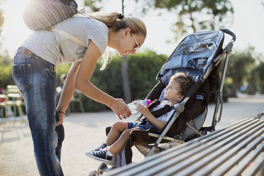 Mutter gibt ihrem Sohn, der im Kinderwagen sitzt, eine Wasserflasche - AZOF00059