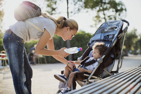 Mutter gibt ihrem Sohn, der im Kinderwagen sitzt, eine Wasserflasche - AZOF00060