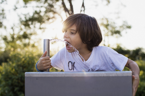 Kleiner Junge trinkt Wasser aus einem Wasserhahn im Freien, lizenzfreies Stockfoto