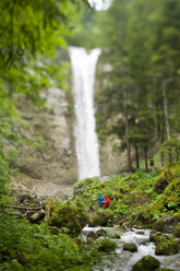 Mann und Frau wandern neben einem malerischen Wasserfall - AURF06596