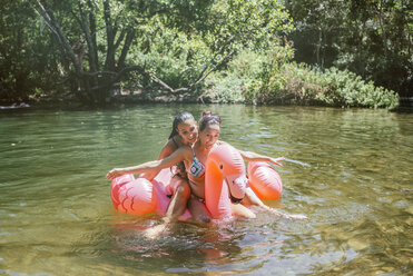 Zwei Freunde planschen im Wasser auf einem schwimmenden Flamingo - KIJF02017
