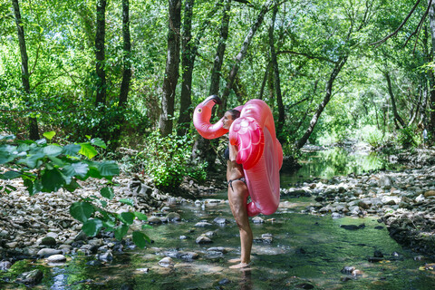 Frau geht im Fluss und trägt einen aufblasbaren Flamingo, lizenzfreies Stockfoto
