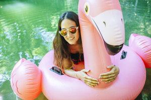 Auf einem aufblasbaren Flamingo auf dem Wasser treibende Frau - KIJF02025