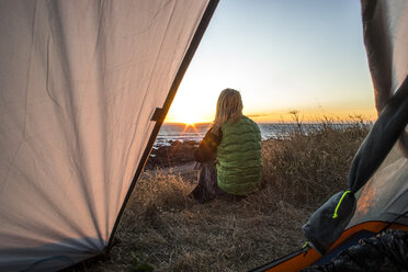 Weiblicher Camper sitzt hinter aufgestelltem Zelt und bewundert die Lost Coast bei Sonnenuntergang, Kalifornien, USA - AURF06847