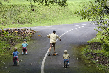 Vater auf Skateboard begleitet Kinder auf Fahrrädern - AURF06869