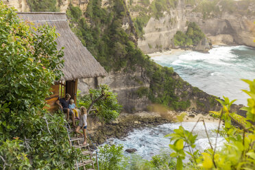 Family on vacations outside thatched roof hut on coastline, Nusa Penida, Bali, Indonesia - AURF06879