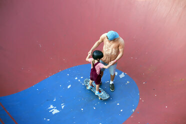 Father supporting daughter on skateboard in skate park, Canggu, Bali, Indonesia - AURF06887