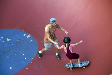 Father supporting daughter on skateboard in skate park, Canggu, Bali, Indonesia - AURF06888