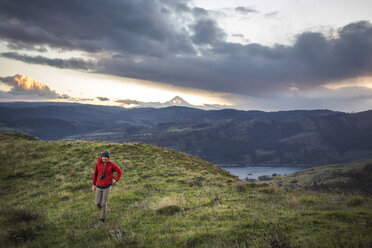 Large clouds over male hiker walking near edge of grassy cliff, Lyle, Oregon, USA - AURF06935