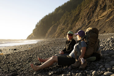 Wanderer ruhen sich bei Sonnenuntergang am Strand aus, während sie auf dem Lost Coast Trail wandern, Kings Range National Conservation Area, Kalifornien, USA - AURF06959